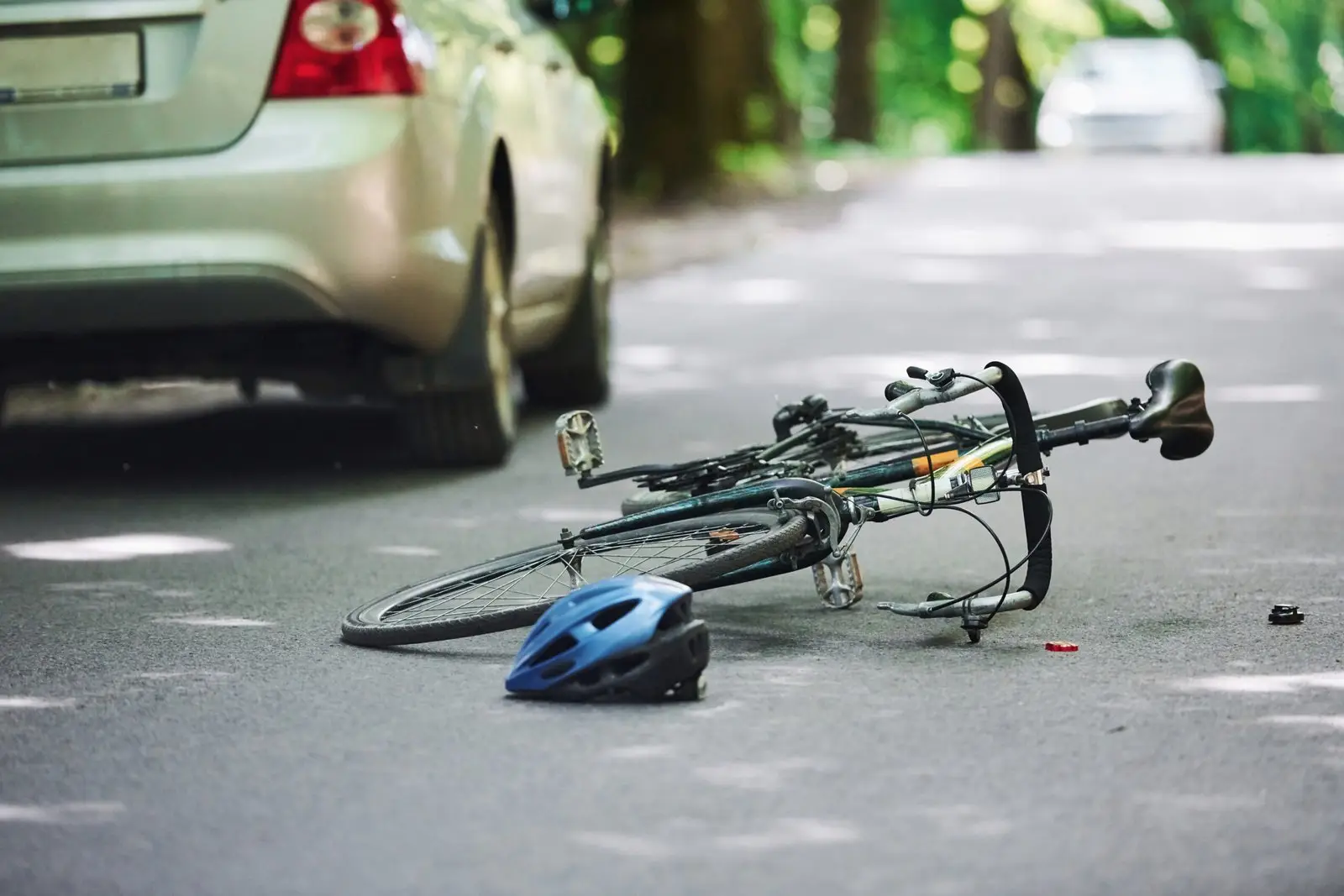 Bicycle lying on the road with a blue helmet beside it after a collision with a car