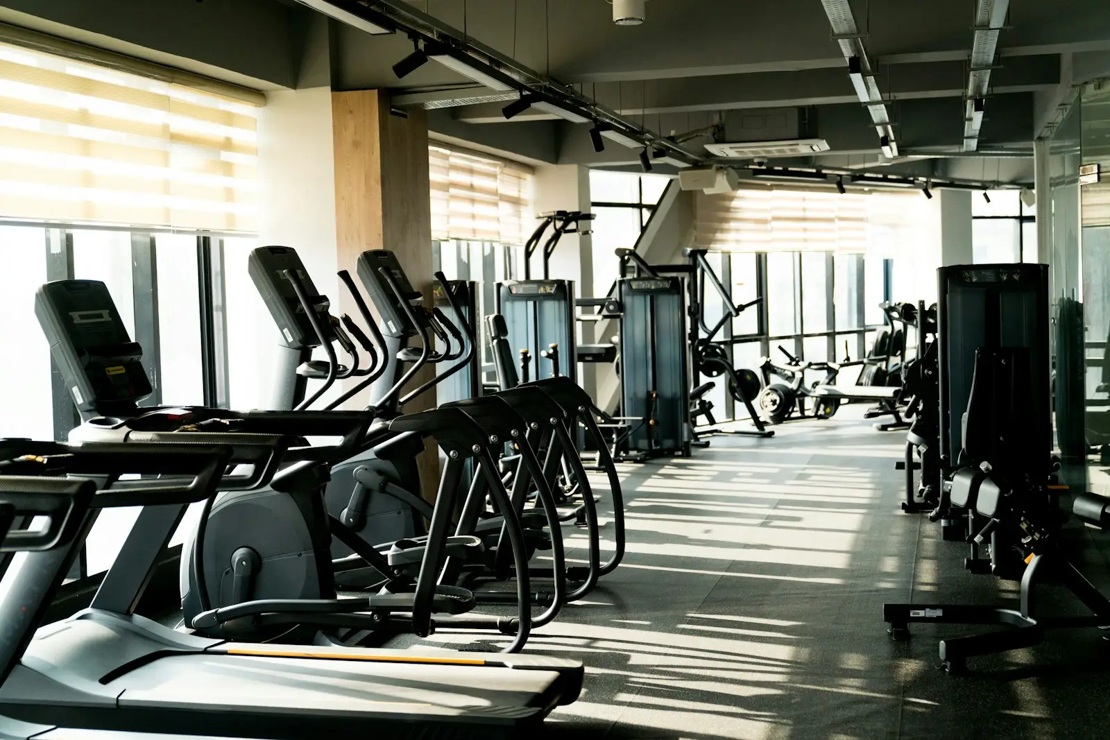 Interior of a modern gym with treadmills, ellipticals, and exercise machines lined up in an empty workout area