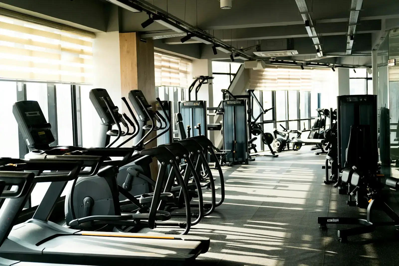 Interior of a modern gym with treadmills, ellipticals, and exercise machines lined up in an empty workout area.