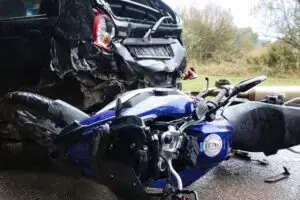 Crashed motorcycle lying on the road after a collision with the rear of a damaged car.