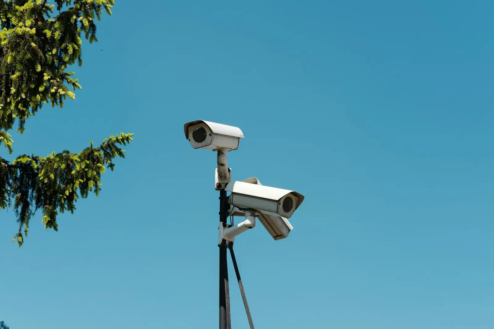 Three outdoor security cameras mounted on a tall pole against a clear blue sky.